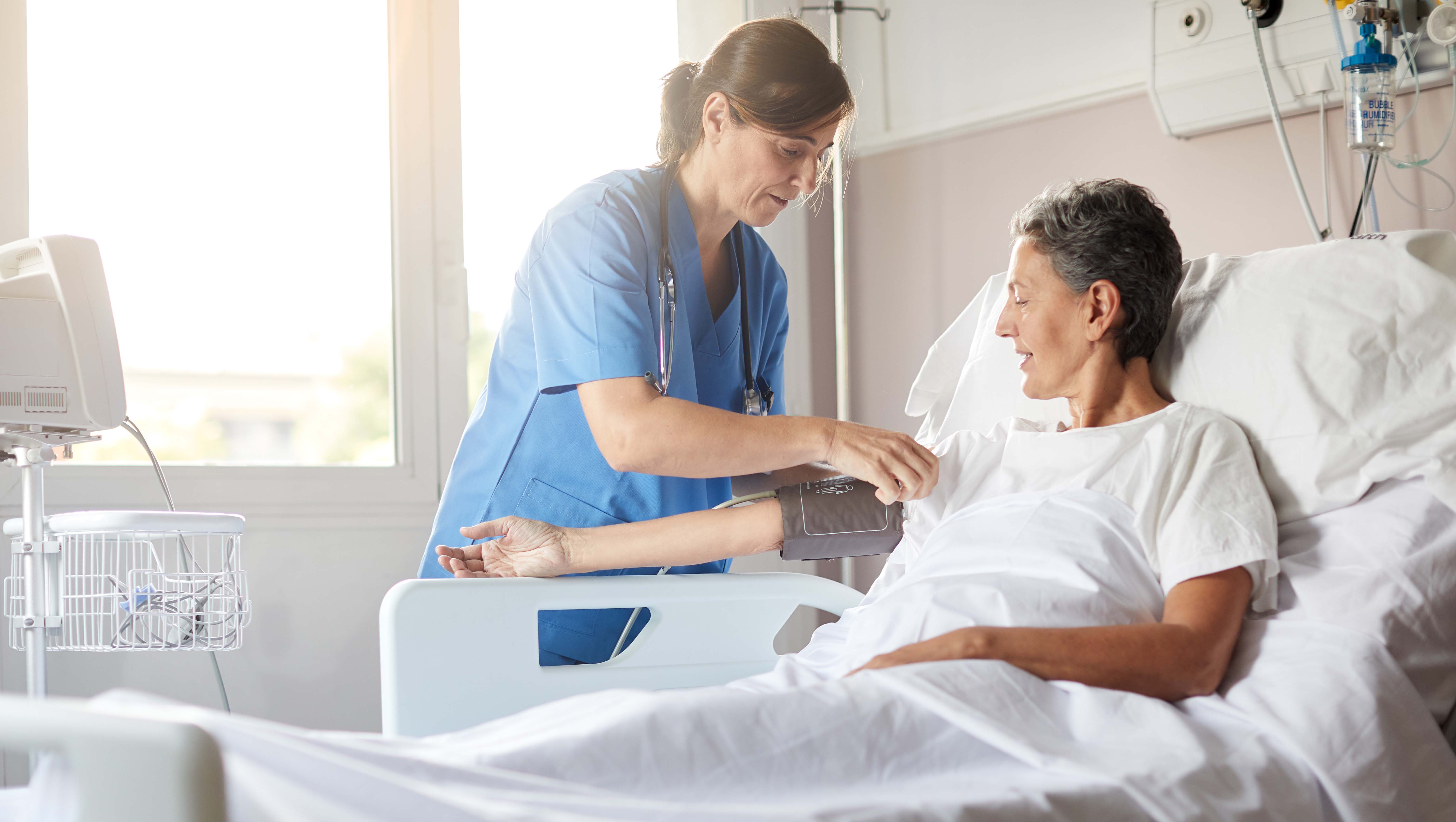 nurse placing blood pressure cuff on patient in hospital bed