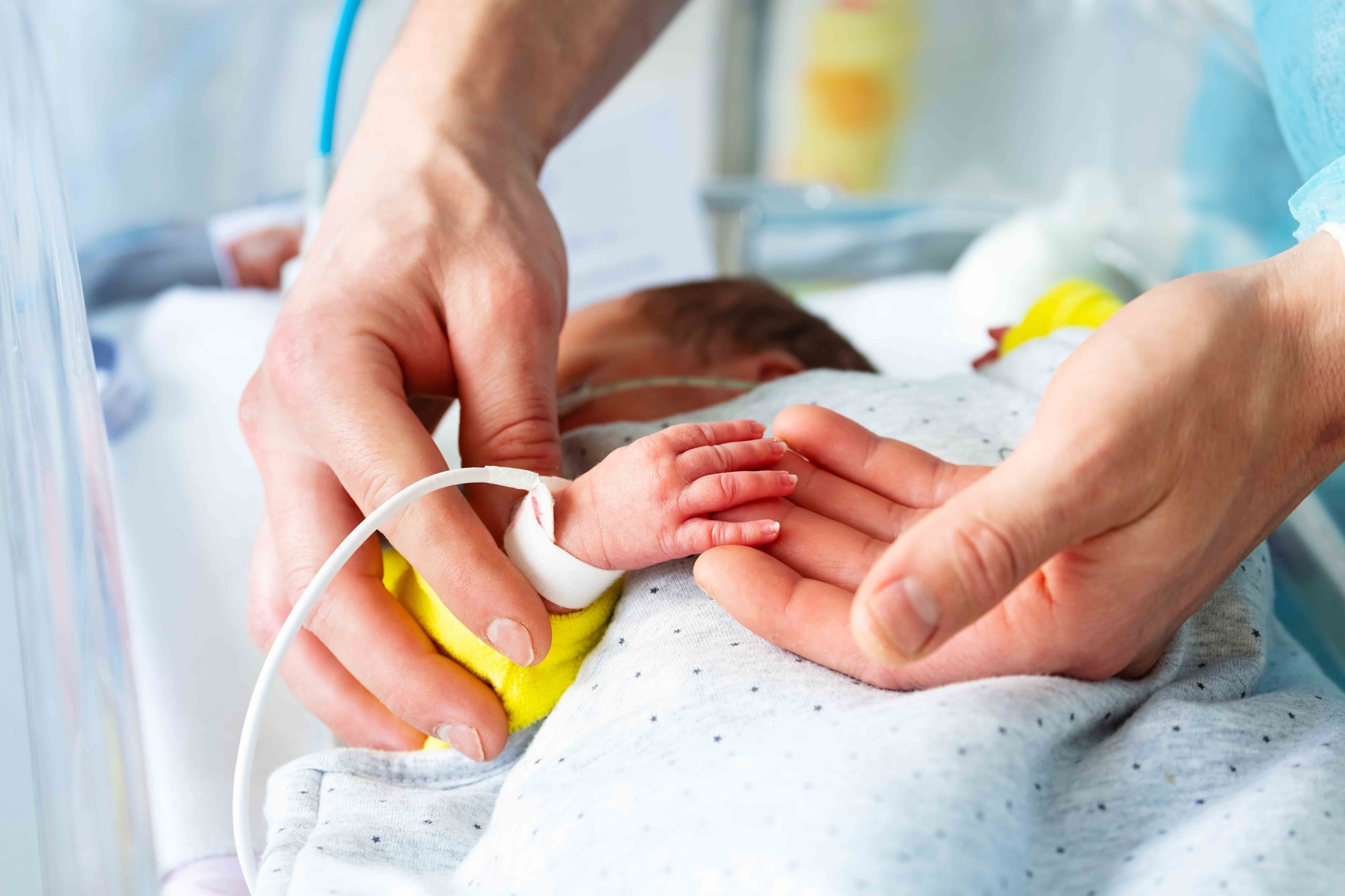 Detail of caregiver or parent holding in their hands the tiny hand of a newborn